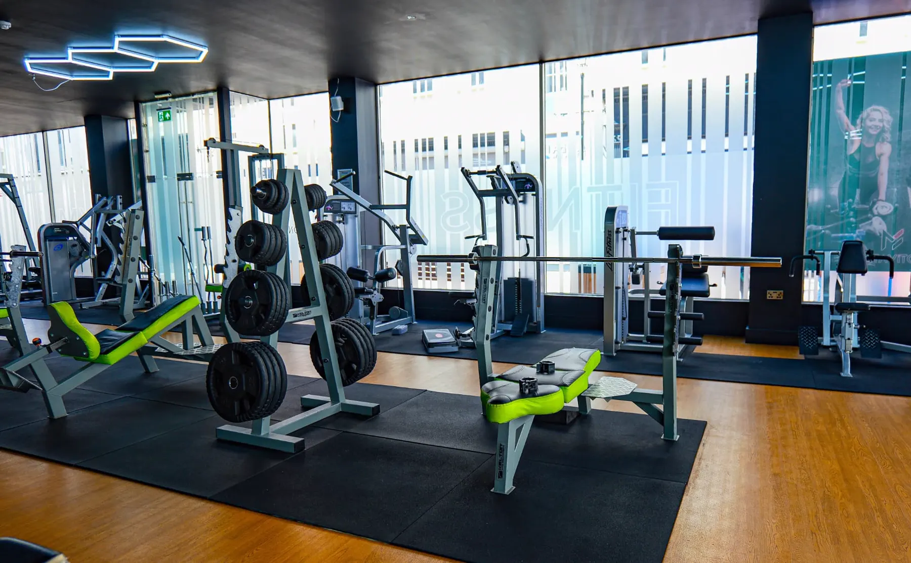 Bench press and squat rack area beside floor-to-ceiling windows